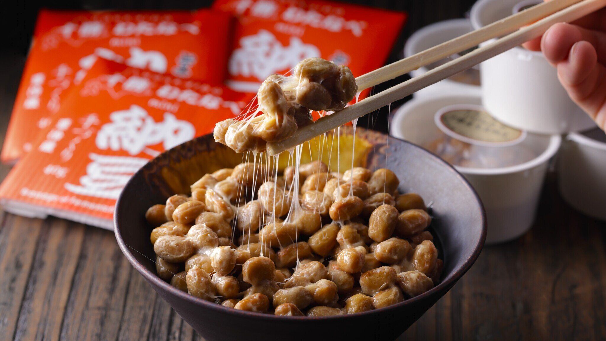 A bowl of chickpeas with a hand holding a pair of chopsticks lifting some chickpeas.