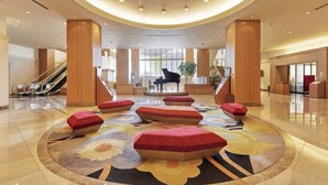 Un vestíbulo espacioso con un piano de cola, asientos acolchados rojos y una alfombra floral en el centro.