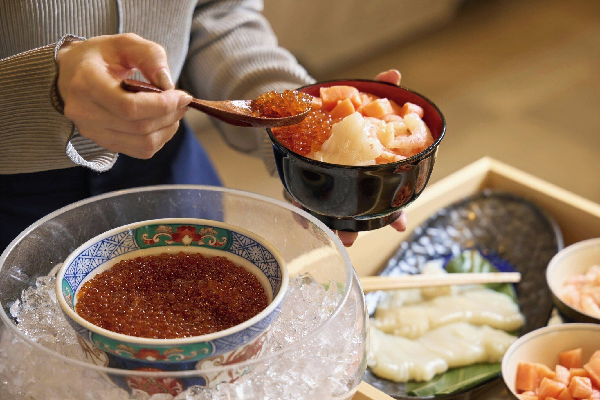 A person holding a bowl with a spoon, ice, and a bowl of red condiment.