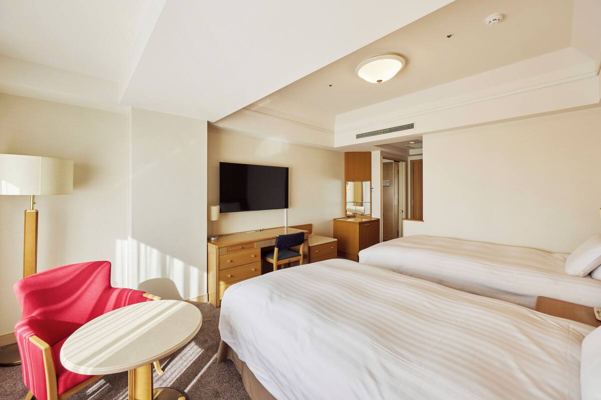 Une chambre d’hôtel avec deux lits, un bureau, une chaise, une télévision et une lampe.