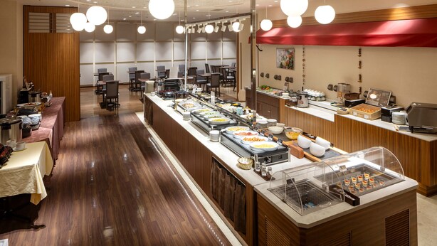 Un buffet proposant divers plats, un espace avec des tables et des chaises, et un comptoir avec une caisse enregistreuse.