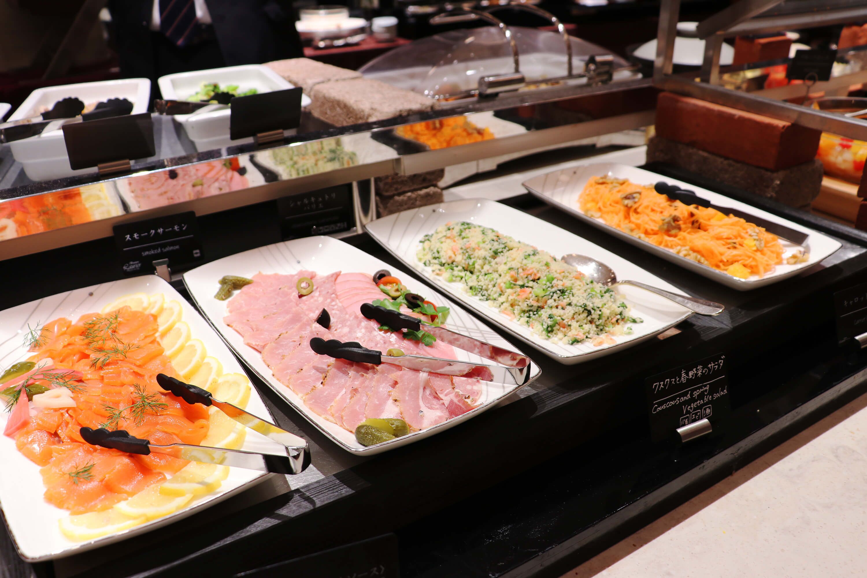 Ein Buffet mit verschiedenen Speisen, darunter Räucherlachs, Schinken und ein Gemischter Salat.