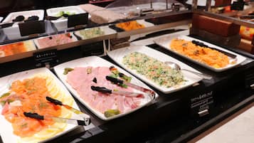 Un bufé con diversas opciones de comida, como salmón ahumado, jamón y una ensalada de verduras.