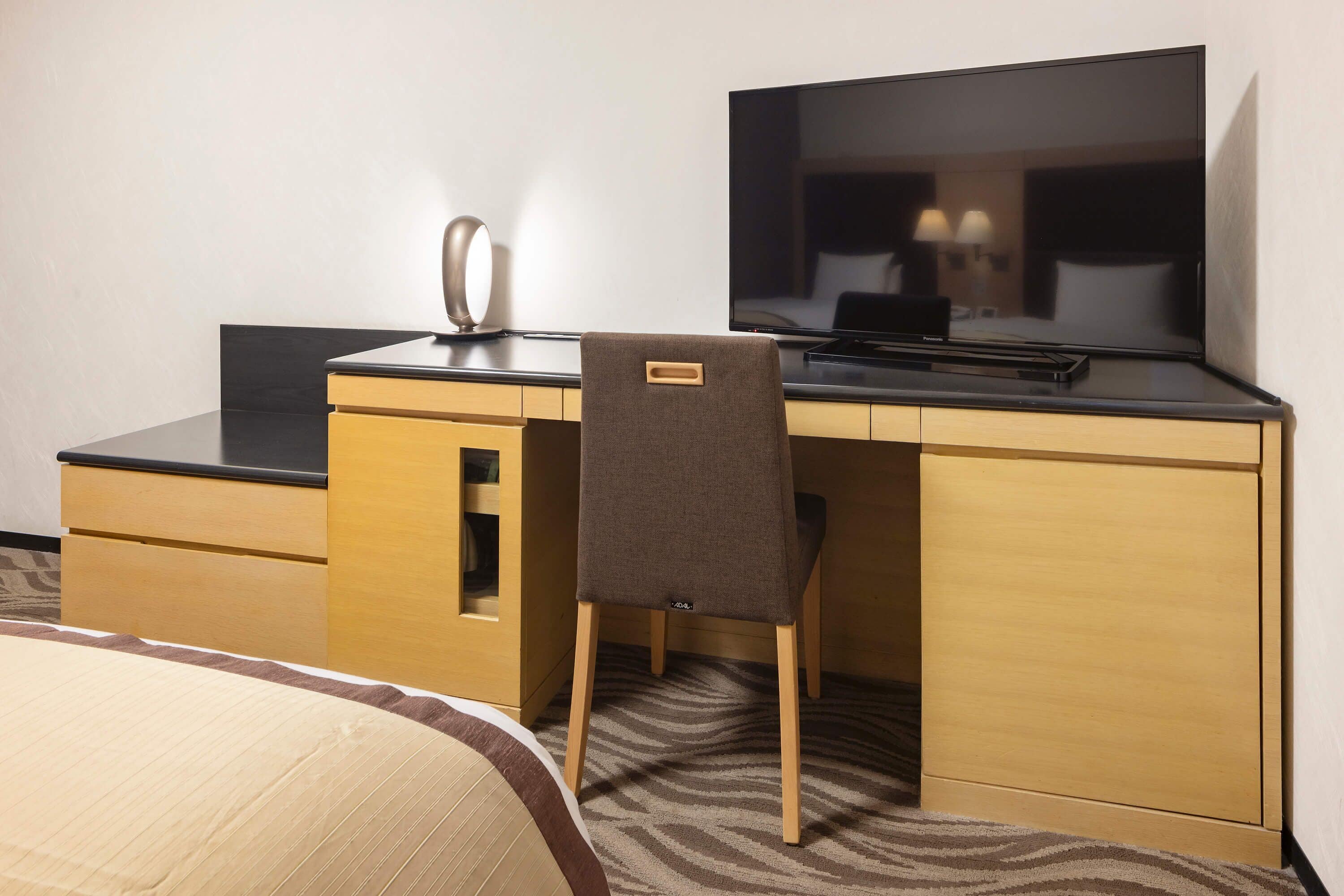 Ein Hotelzimmer mit Bett, Schreibtisch mit Flachbildfernseher, Stuhl und Spiegel.