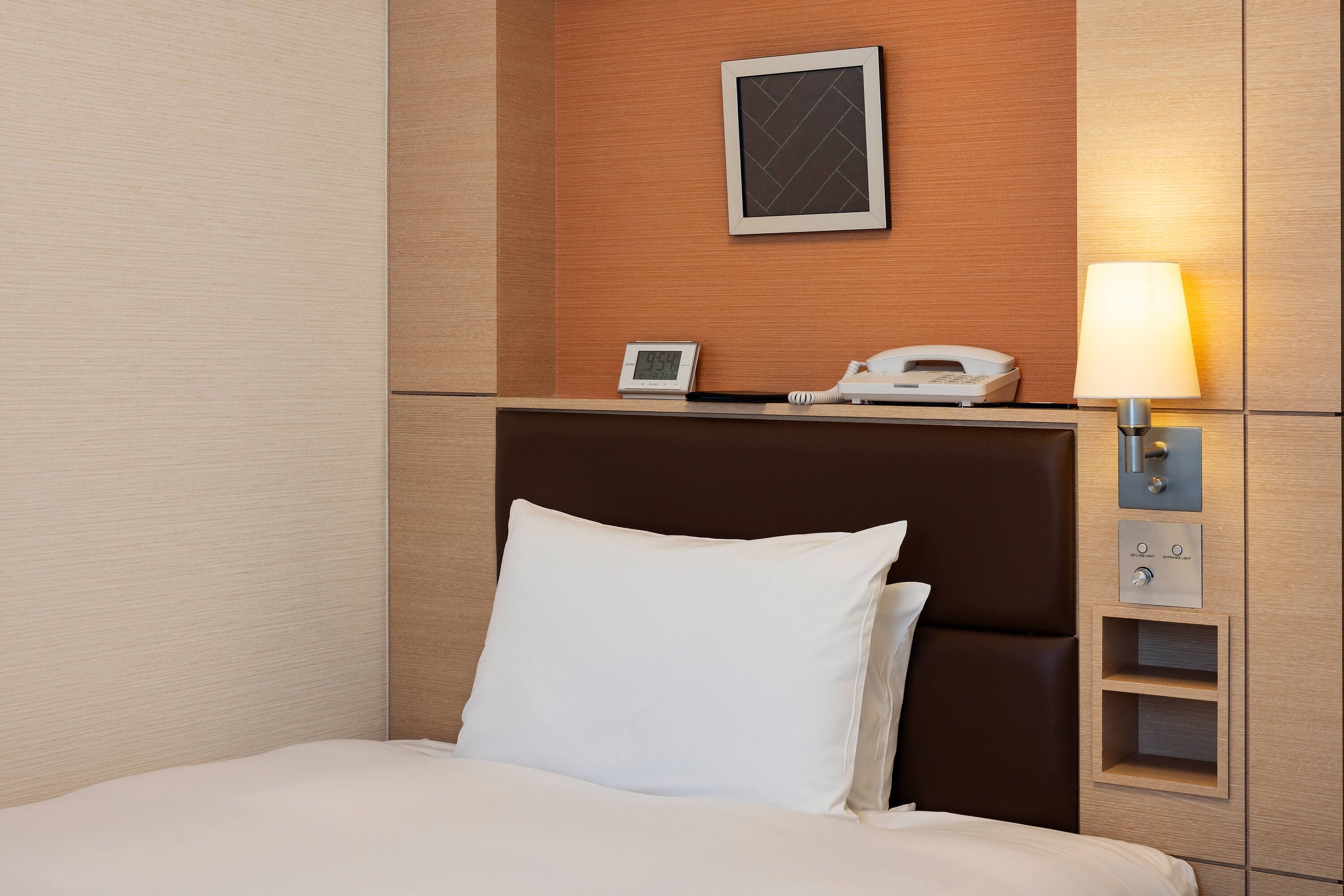 Een hotelkamer met een bed, een nachtkastje met een lamp, een telefoon en een digitale klok.