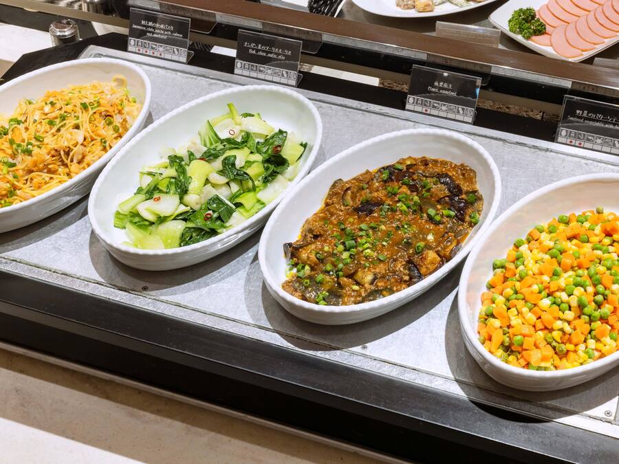 Buffet com diversos pratos, incluindo macarrão, salada de legumes, prato com carne e um mix de vegetais.