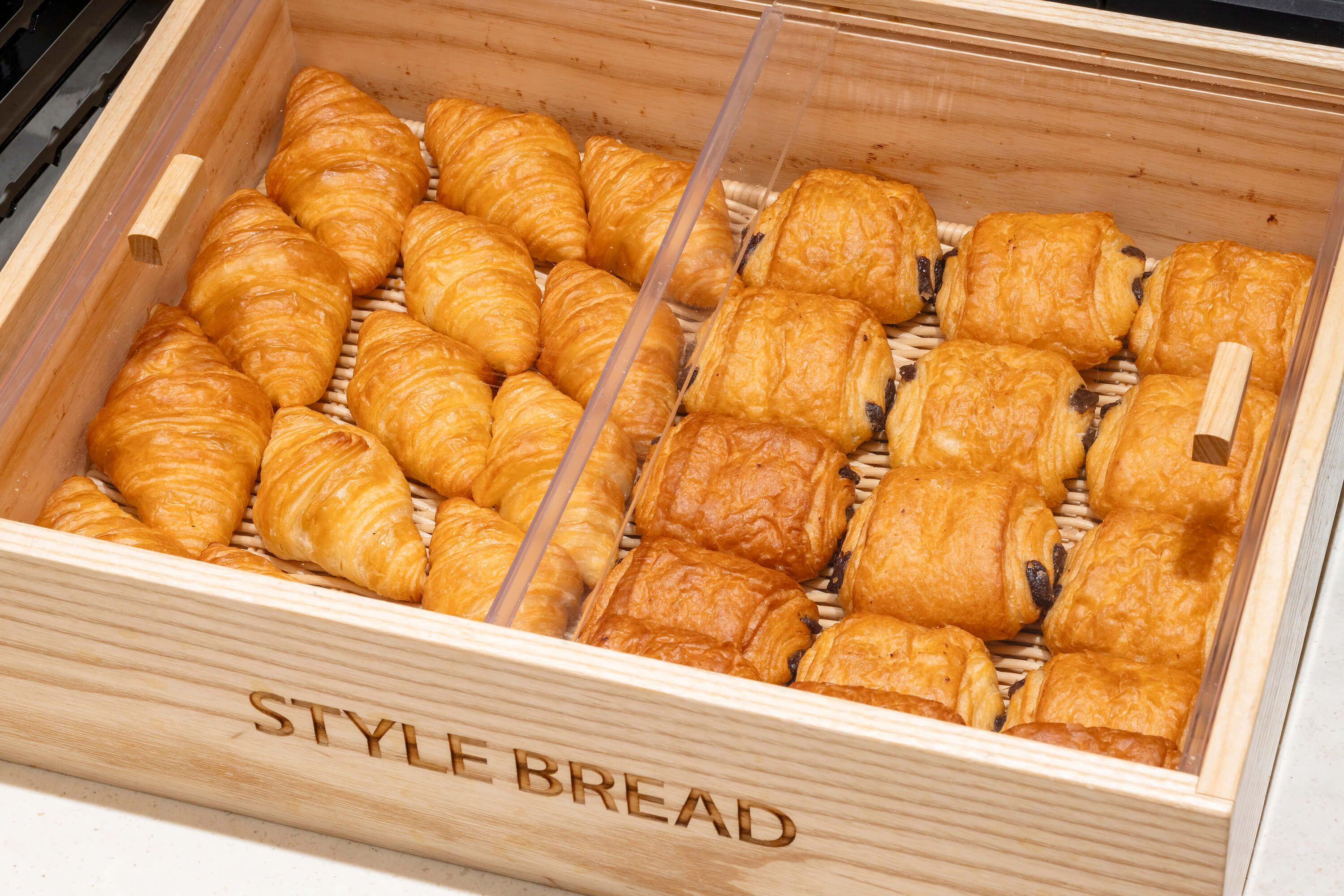 Een houten doos met de tekst 'STYLE BREAD' en daarin verschillende soorten croissants.