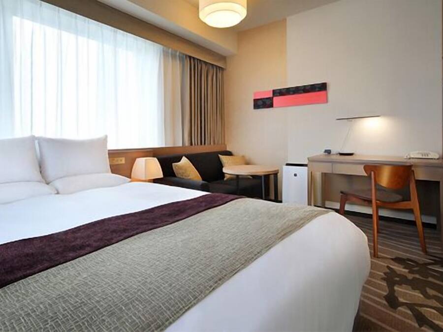 A hotel room with a large bed, a desk, and a chair.