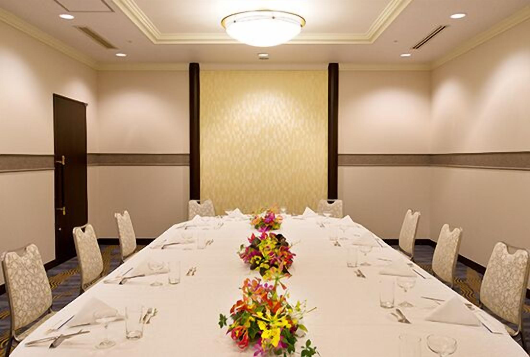 A conference room with a long table set for a meeting, surrounded by chairs, and a decorative floral centerpiece.