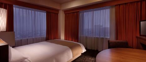 A hotel room with a large bed, a desk, a chair, and a television.