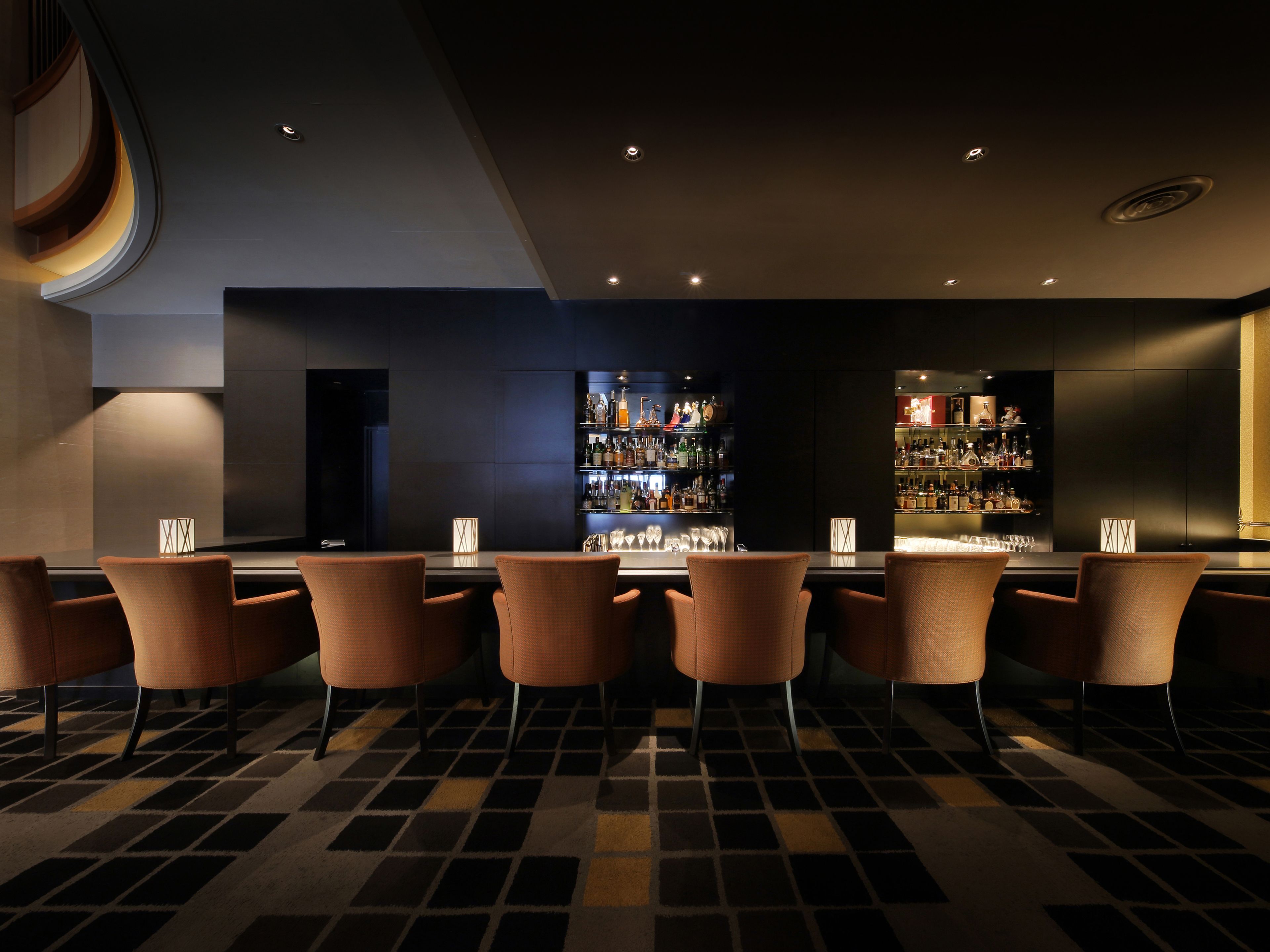 A bar area with a long counter, multiple bar stools, and a well-stocked bar with various bottles and glasses.