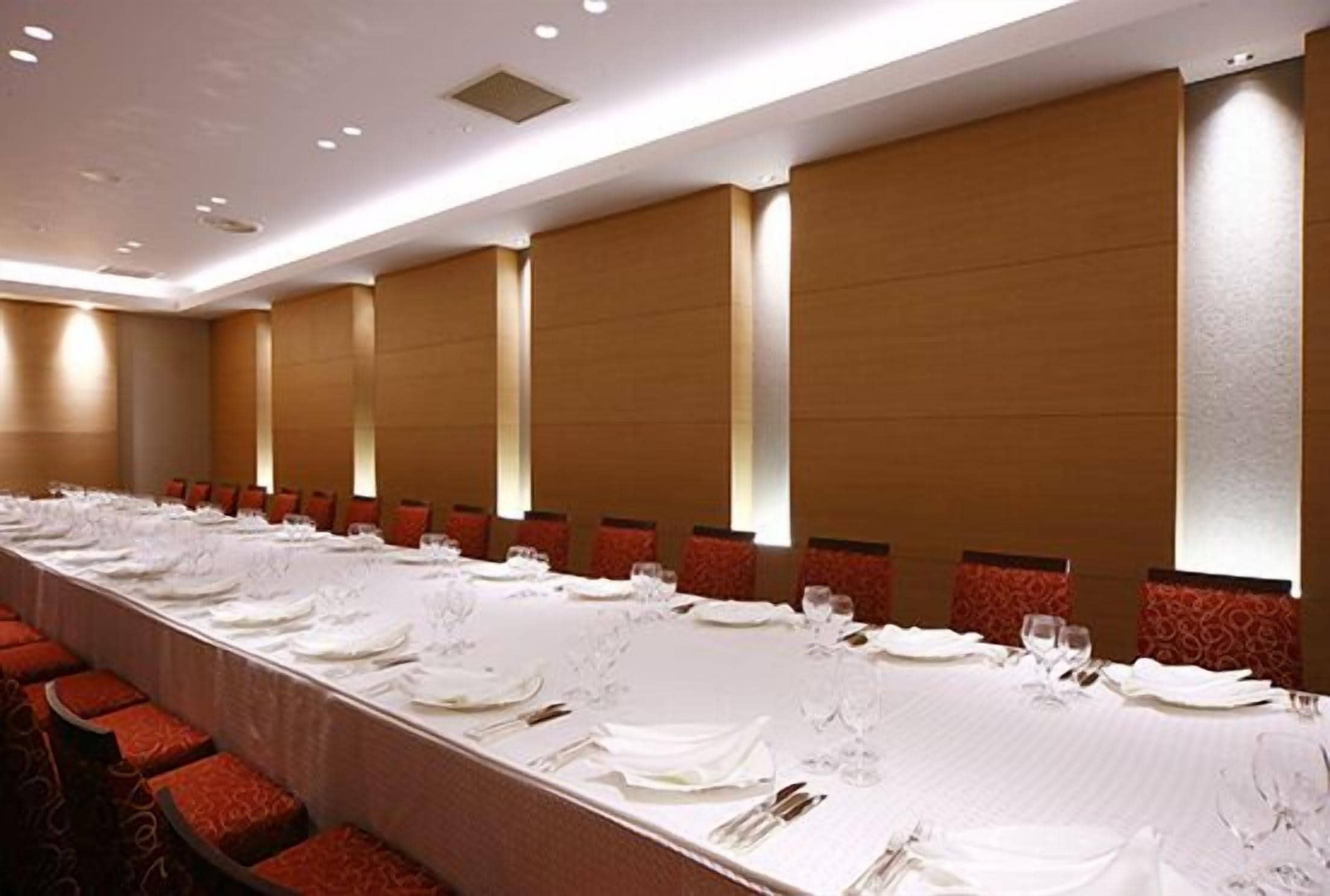 A conference room with a long table set for a meeting, red upholstered chairs, and recessed lighting.