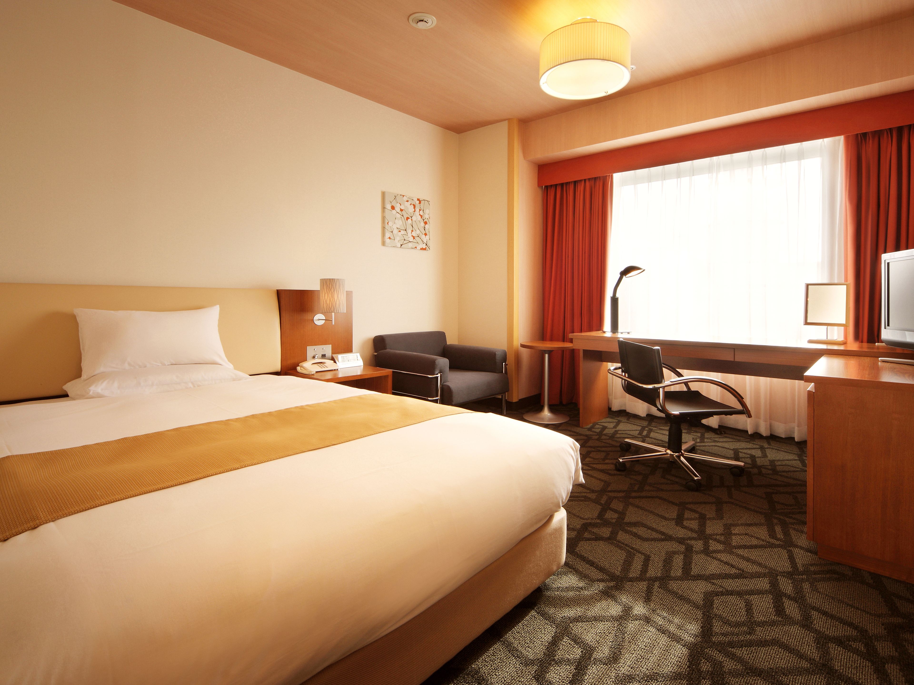 Ein Hotelzimmer mit einem großen Bett, einem Schreibtisch mit Stuhl, einem Fernseher und einem Fenster mit Vorhängen.