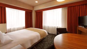 Een hotelkamer met een bed, een bureau, een stoel, een televisie en een groot raam met gordijnen.