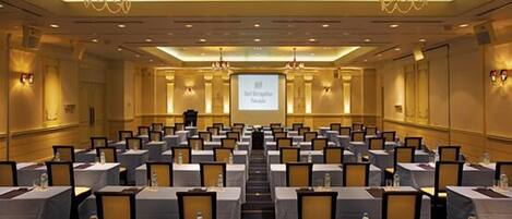A conference room with rows of tables, chairs, and a projector screen at the front.