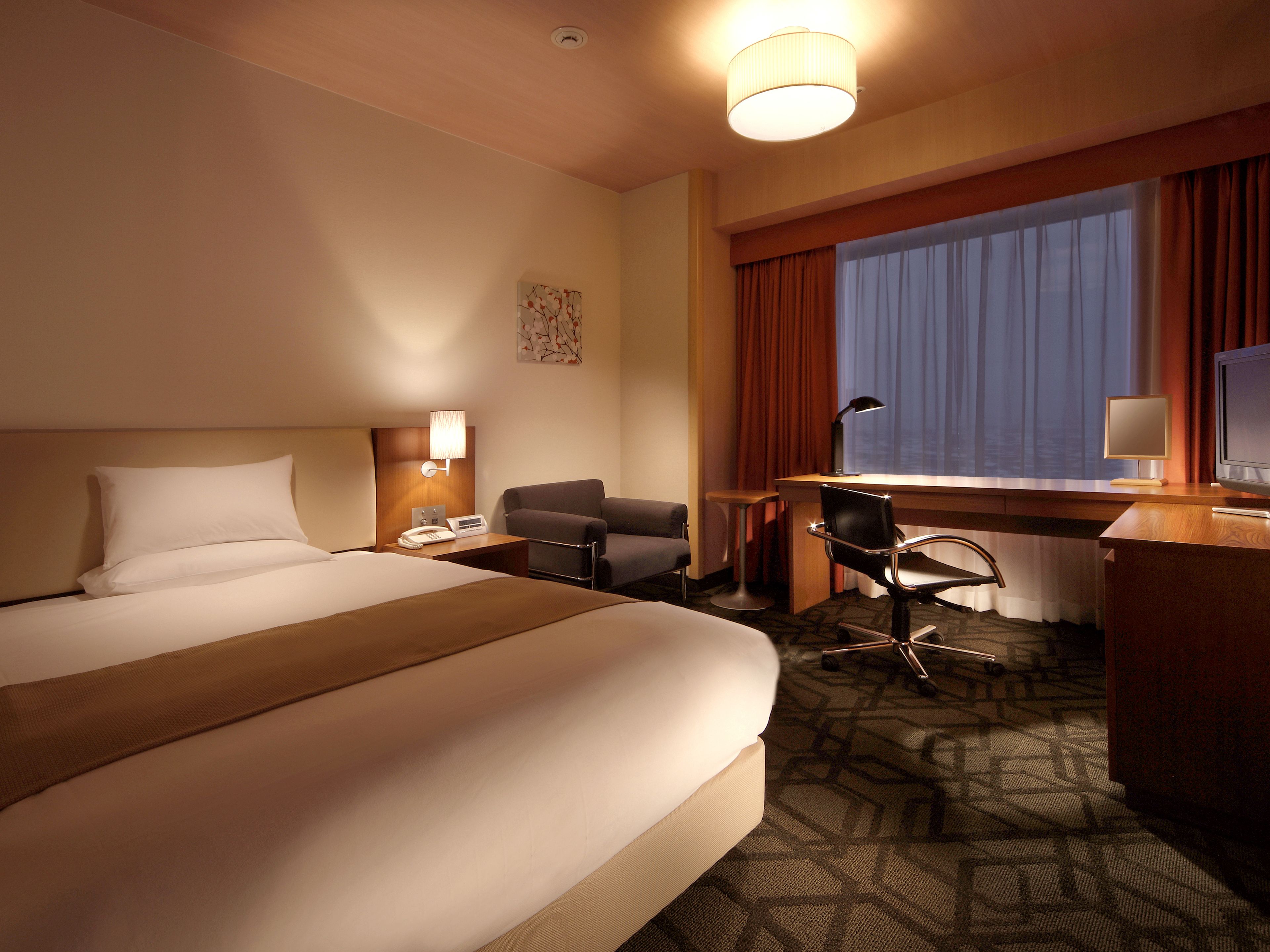 Una habitación de hotel con una cama grande, un escritorio con una computadora, una silla y una lámpara.