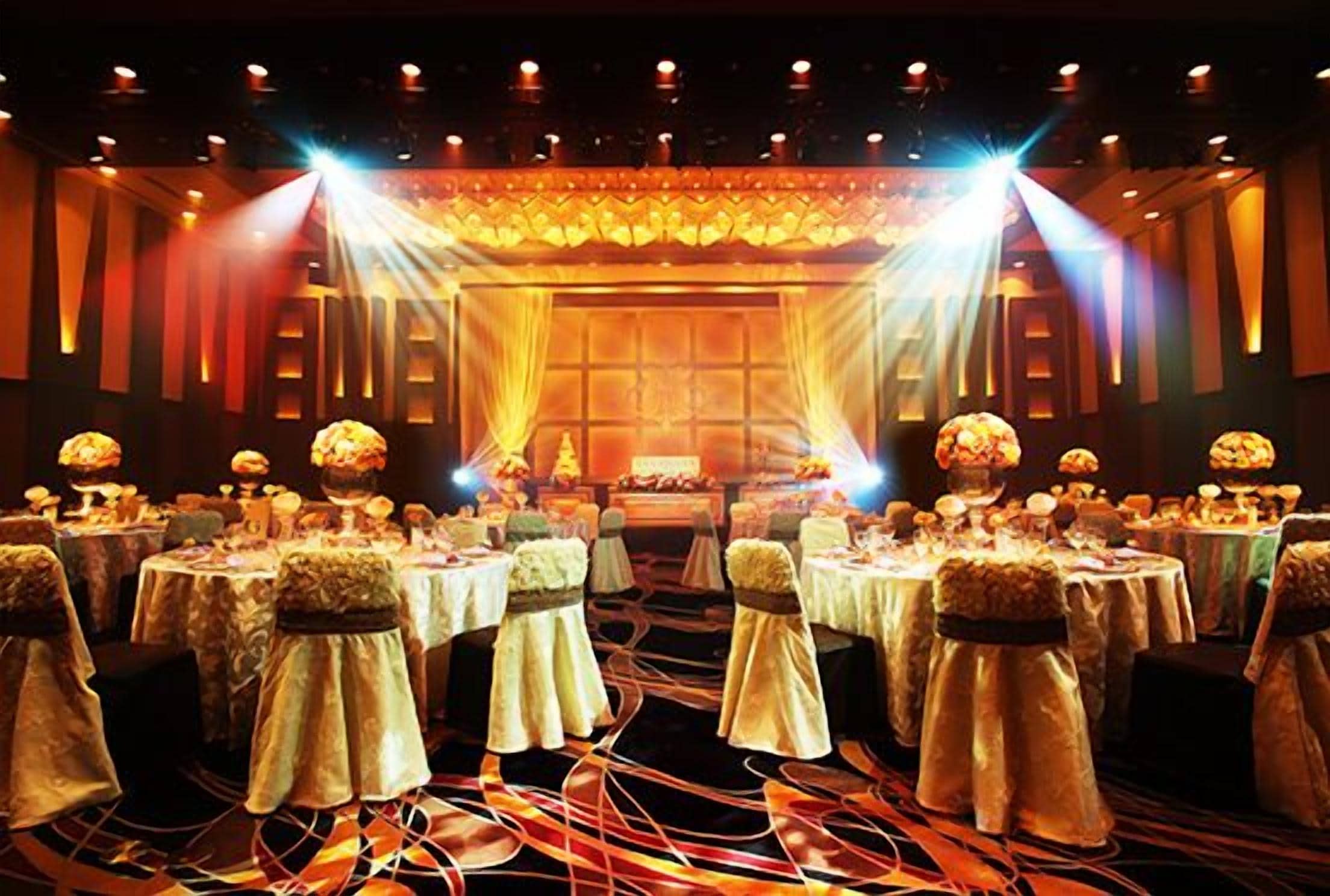 A banquet hall with round tables, chairs with headpieces, and a stage with lighting.