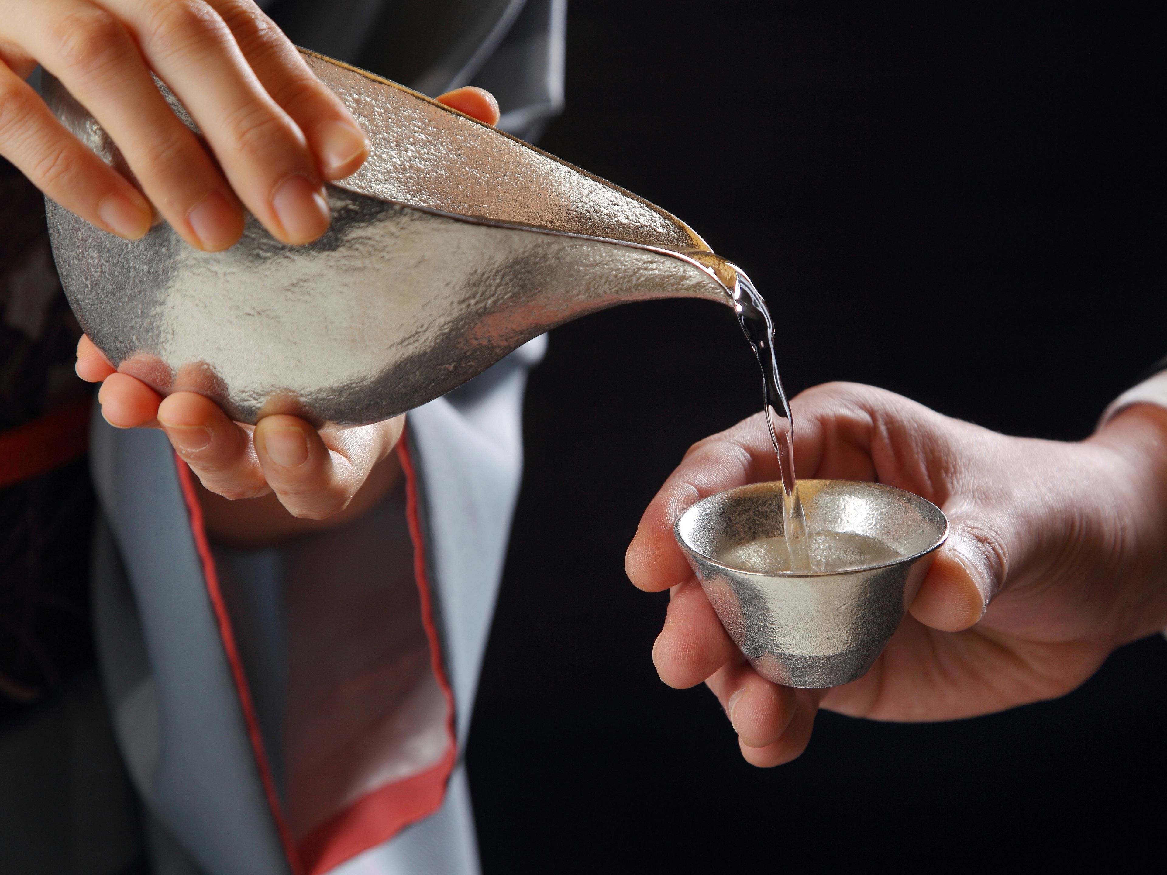 A person pouring water from a metal pitcher into a metal cup.