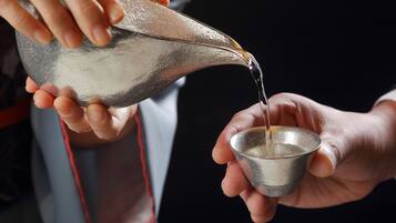 A person pouring water from a metal pitcher into a metal cup.