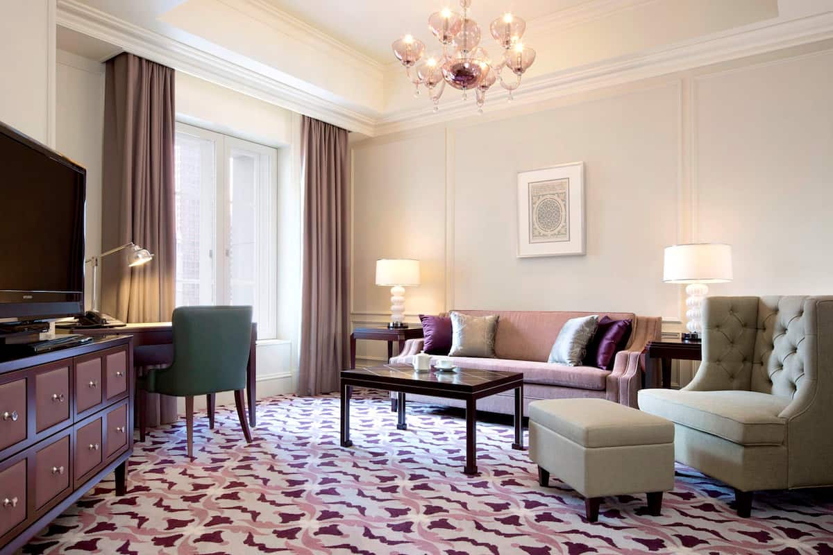 Habitación de hotel con televisión, sofá, sillón, mesa de centro y alfombra estampada.