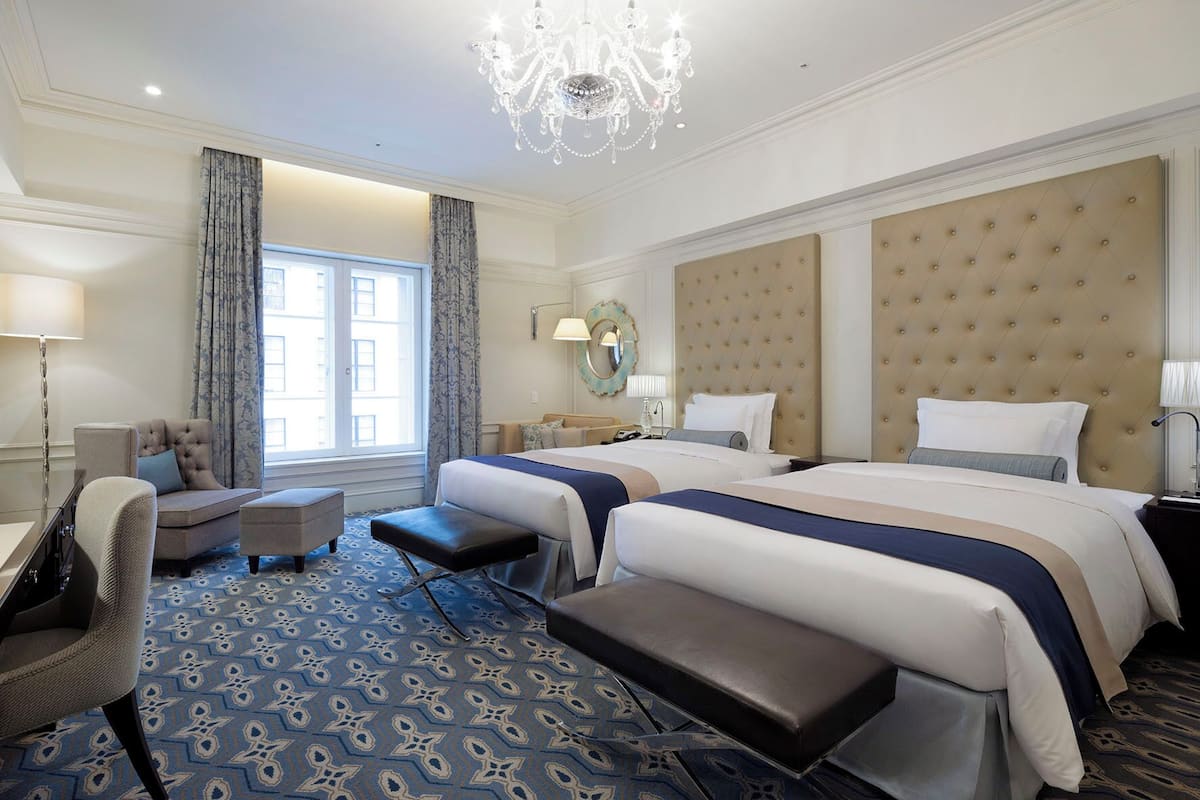 Habitación de hotel con dos camas, un candelabro, un ventanal grande y una alfombra estampada.