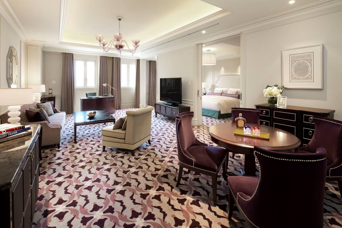 Una habitación de hotel con una cama grande, un área de estar con un sofá y sillones, una mesa de comedor con sillas, un televisor y un escritorio con una computadora.