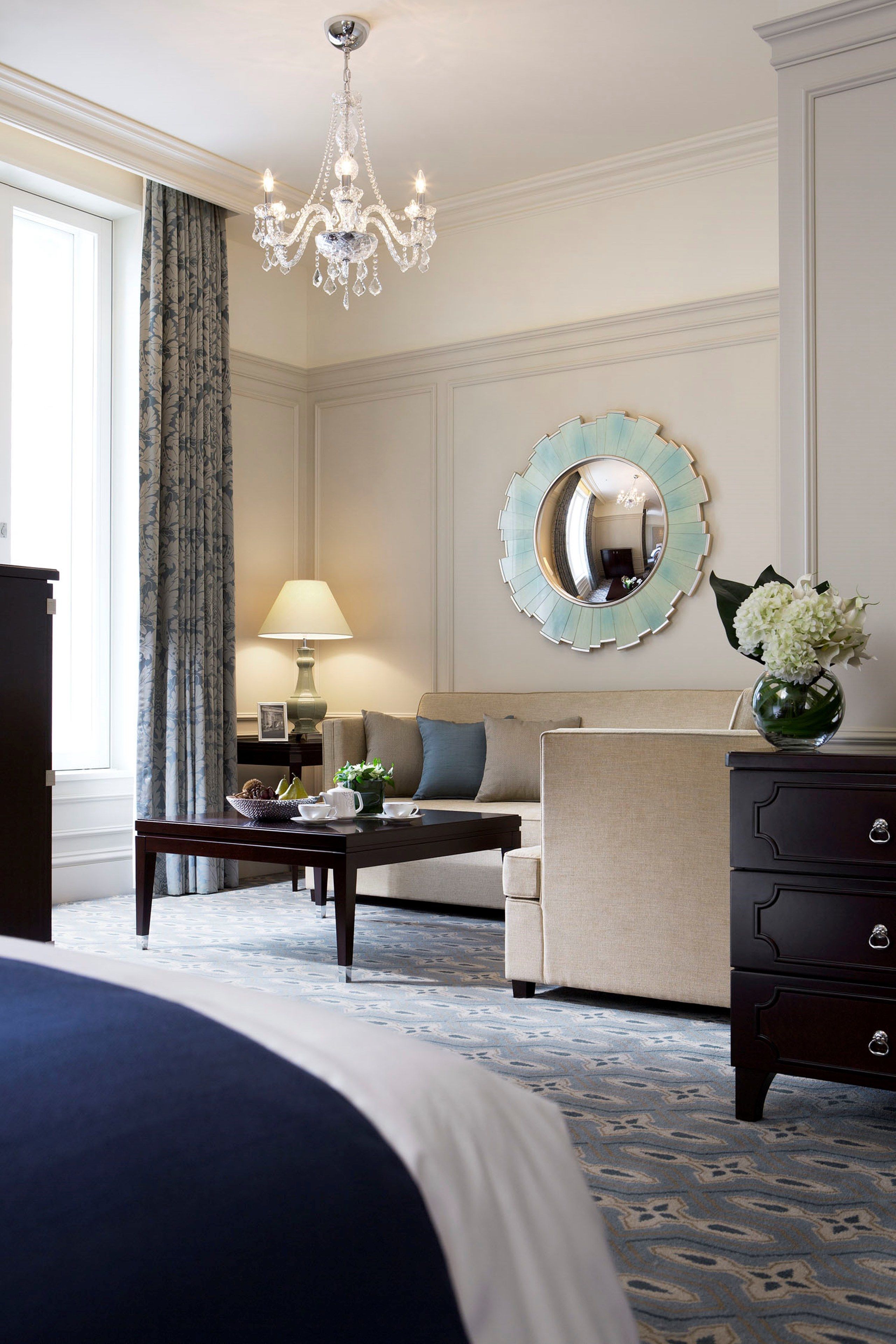 A hotel room with a bed, a sofa, a coffee table, a dresser, a mirror, and a chandelier.