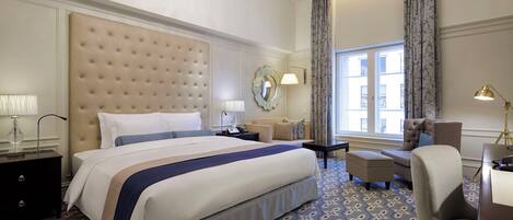A hotel room with a large bed, a chandelier, a sofa, a chair, and a desk.