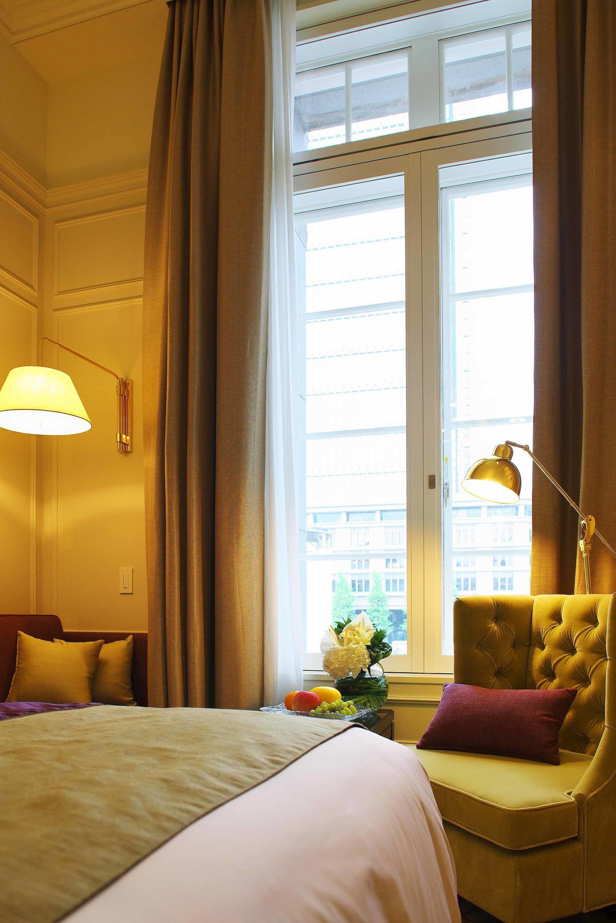 A hotel room with a large bed, a sitting area with a chair, a lamp, and a window with curtains.