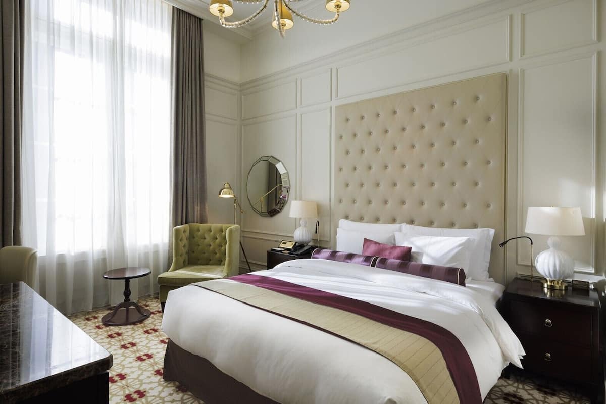 Una habitación de hotel con una cama grande, un espejo redondo, un sillón verde, una mesita y un escritorio.