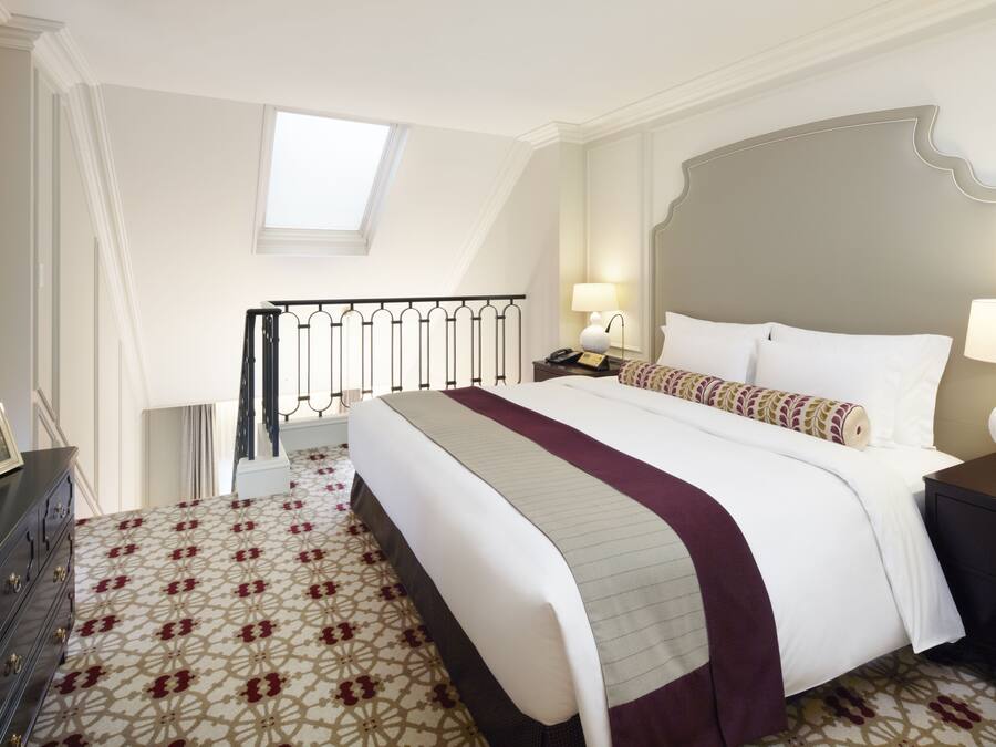 A hotel room with a large bed, a nightstand with lamps, a dresser, and a patterned carpet.