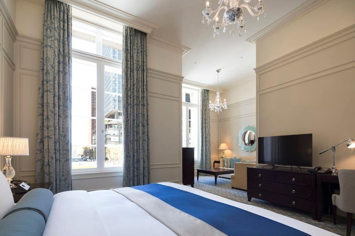 Et hotelværelse med en stor seng, et skrivebord, et fjernsyn og udsigt over bybilledet.