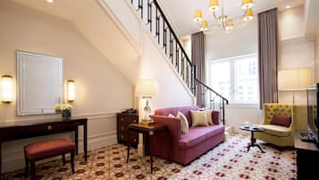 A hotel room with a staircase, a sofa, a bench, a desk, and a television.
