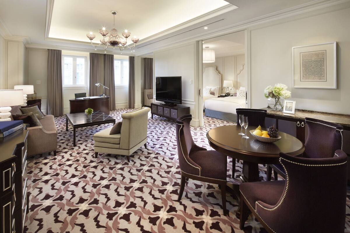 Habitación de hotel con una cama grande, televisión, escritorio con computadora, mesa de comedor con sillas y alfombra estampada.