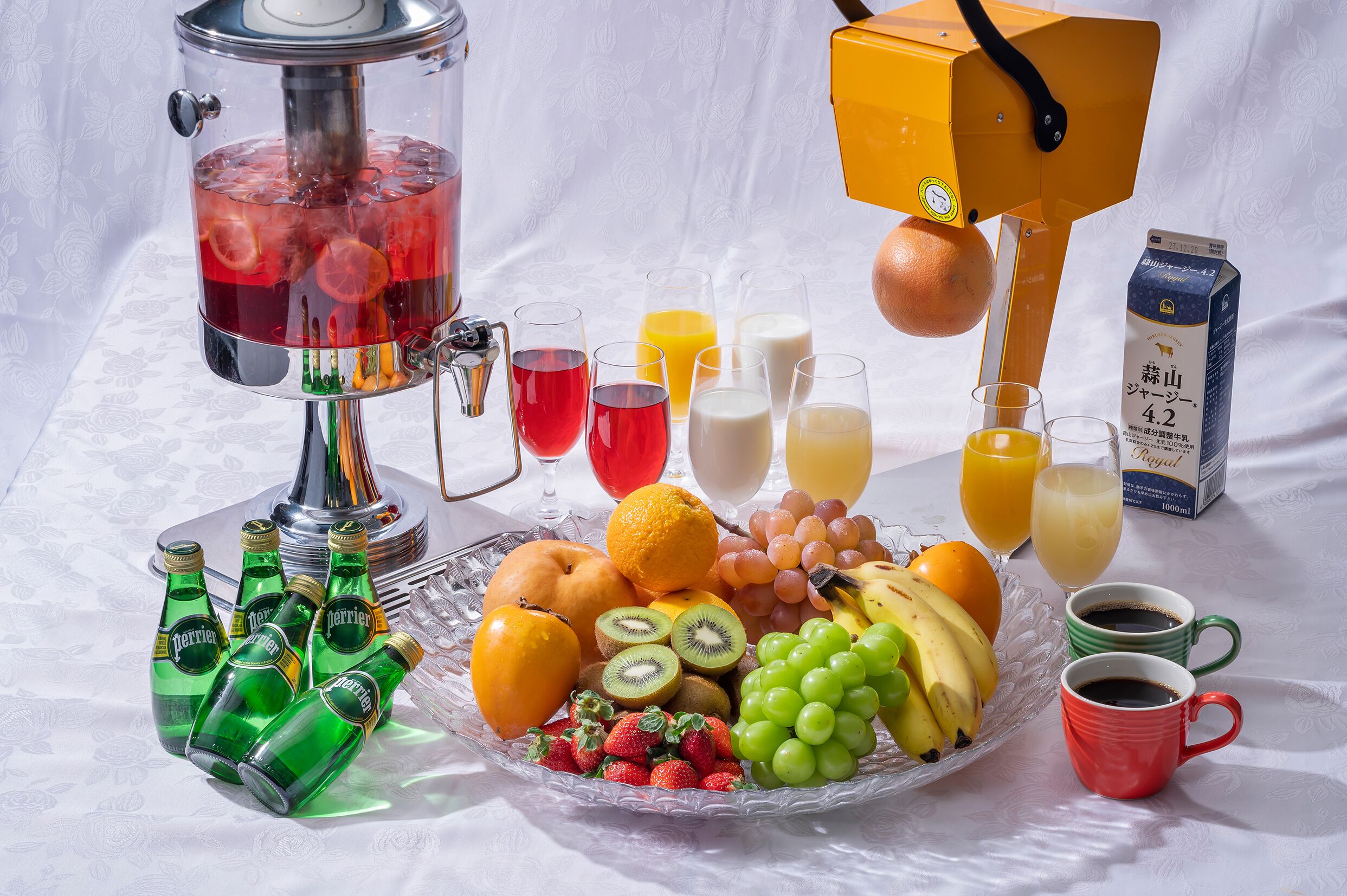 Una estación de bebidas con dispensador, una bandeja de frutas y botellas de agua Perrier.