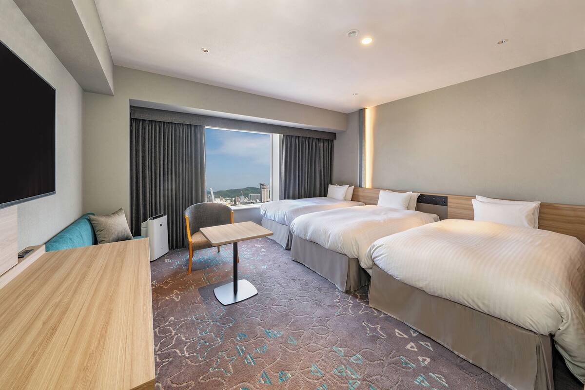 A hotel room with a large bed, a smaller bed, a sofa, a TV, and a view of the city.