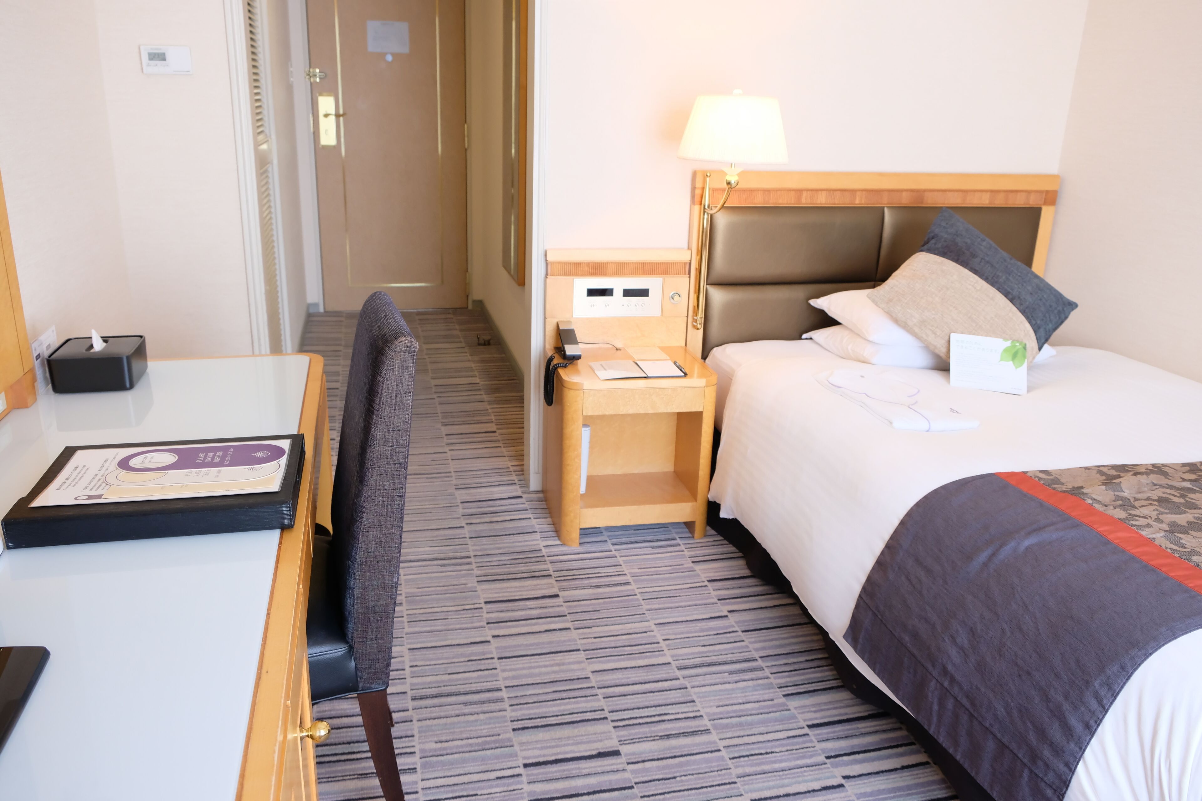 Una habitación de hotel con cama, mesita de noche, lámpara y escritorio con silla.