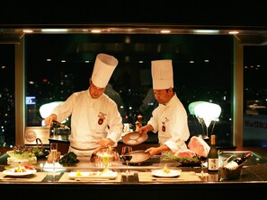 Two chefs in white uniforms preparing food at a counter with various dishes and drinks. - Hotel Granvia Okayama (Okayama)