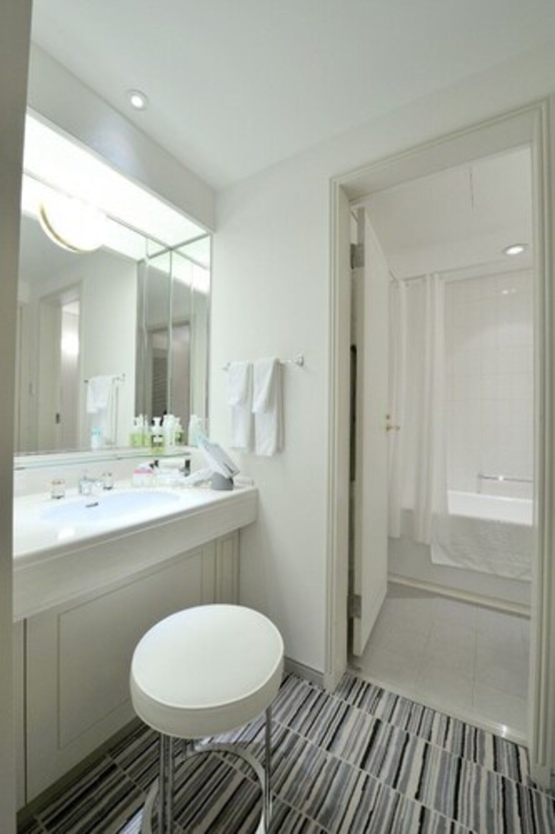 Un baño moderno con un espejo grande, lavamanos blanco y un taburete redondo.