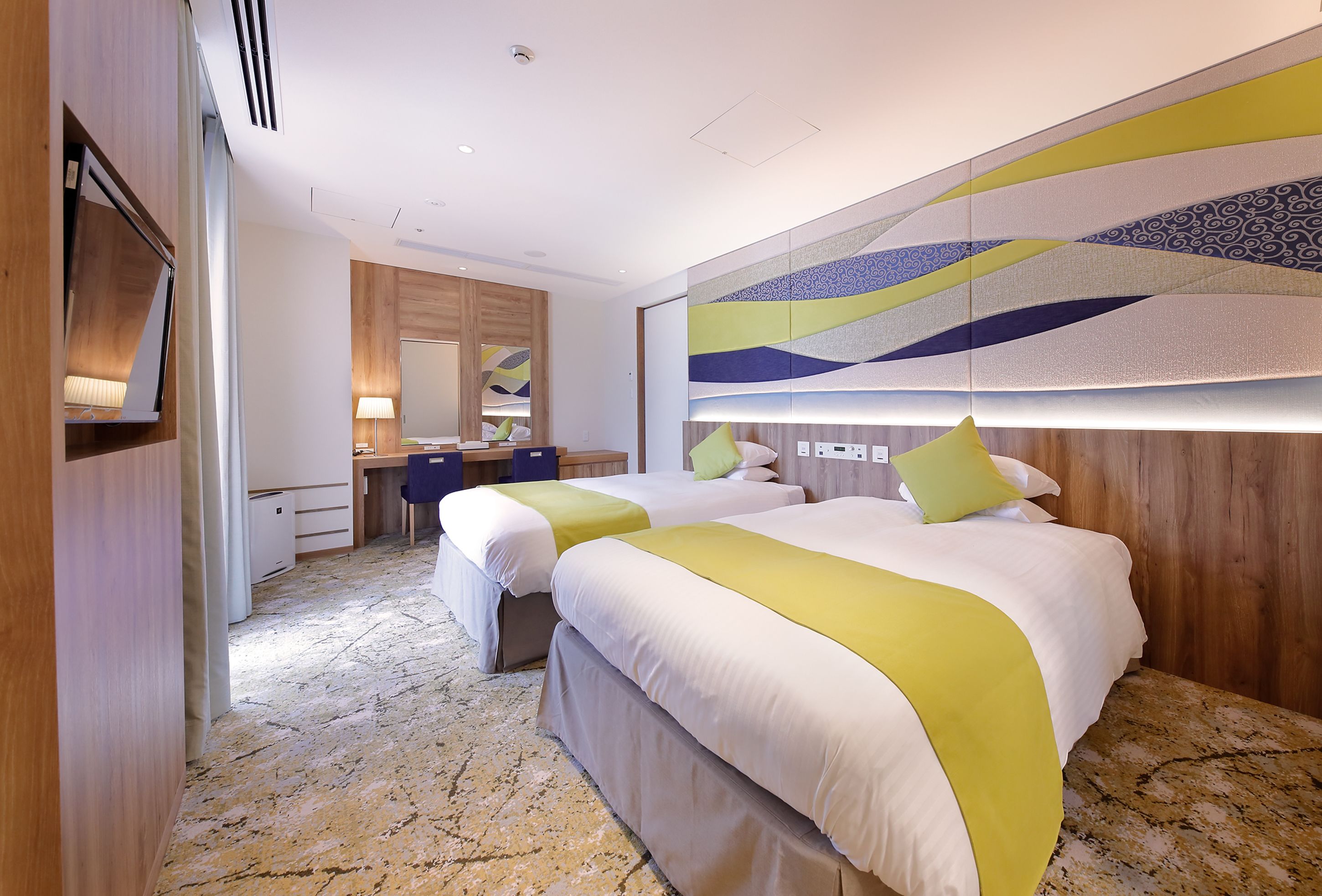 A hotel room with two beds, a desk, a chair, and a large abstract wall decoration.