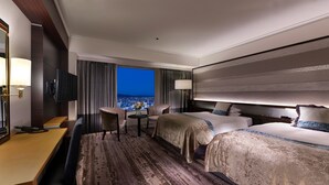 Habitación de hotel con una cama grande, un escritorio y una silla. Hay un televisor montado en la pared y una ventana con vistas a la ciudad.