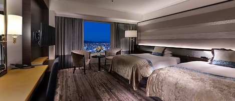 A hotel room with a large bed, a desk, and a chair. There is a TV mounted on the wall and a window with a view of the city.
