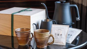 A table with two ceramic mugs, a black kettle, a box, and a coffee bag.