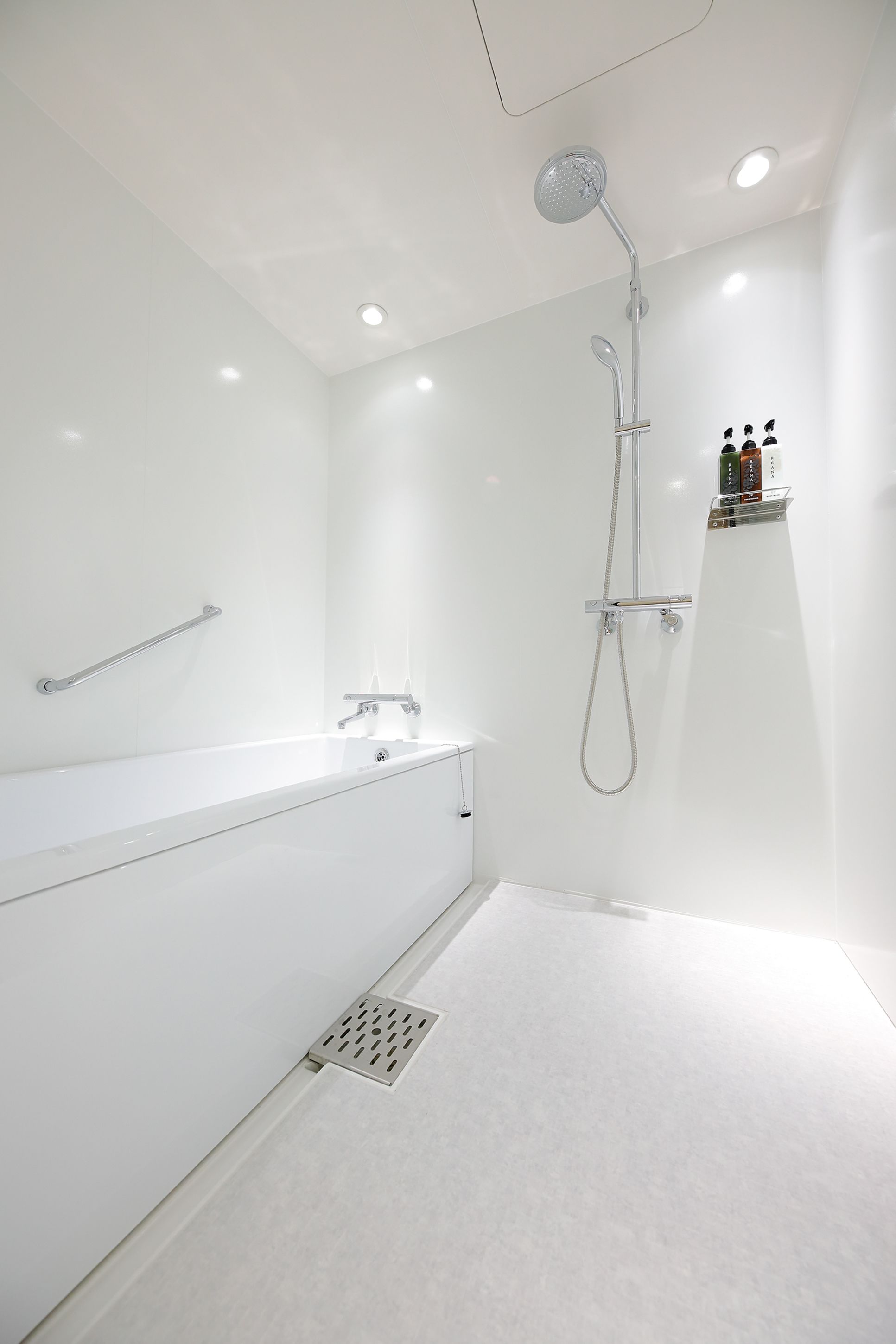A modern bathroom with a white bathtub, a shower with a handheld showerhead, and a wall-mounted shelf with toiletries.