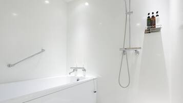 A modern bathroom with a white bathtub, a shower with a handheld showerhead, and a wall-mounted shelf with toiletries.