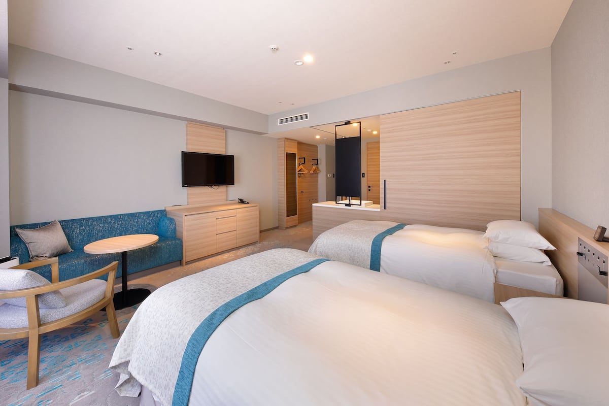 A modern hotel room with two beds, a sofa, a small table, and a TV.