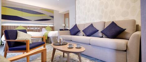 Una habitación de hotel moderna con un sofá, un sillón y una pequeña mesa con tetera y tazas.