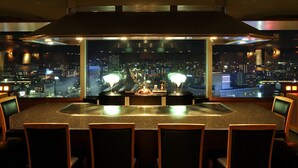 Zona de bar con vista a la ciudad, varias sillas y una mesa central con una lámpara.
