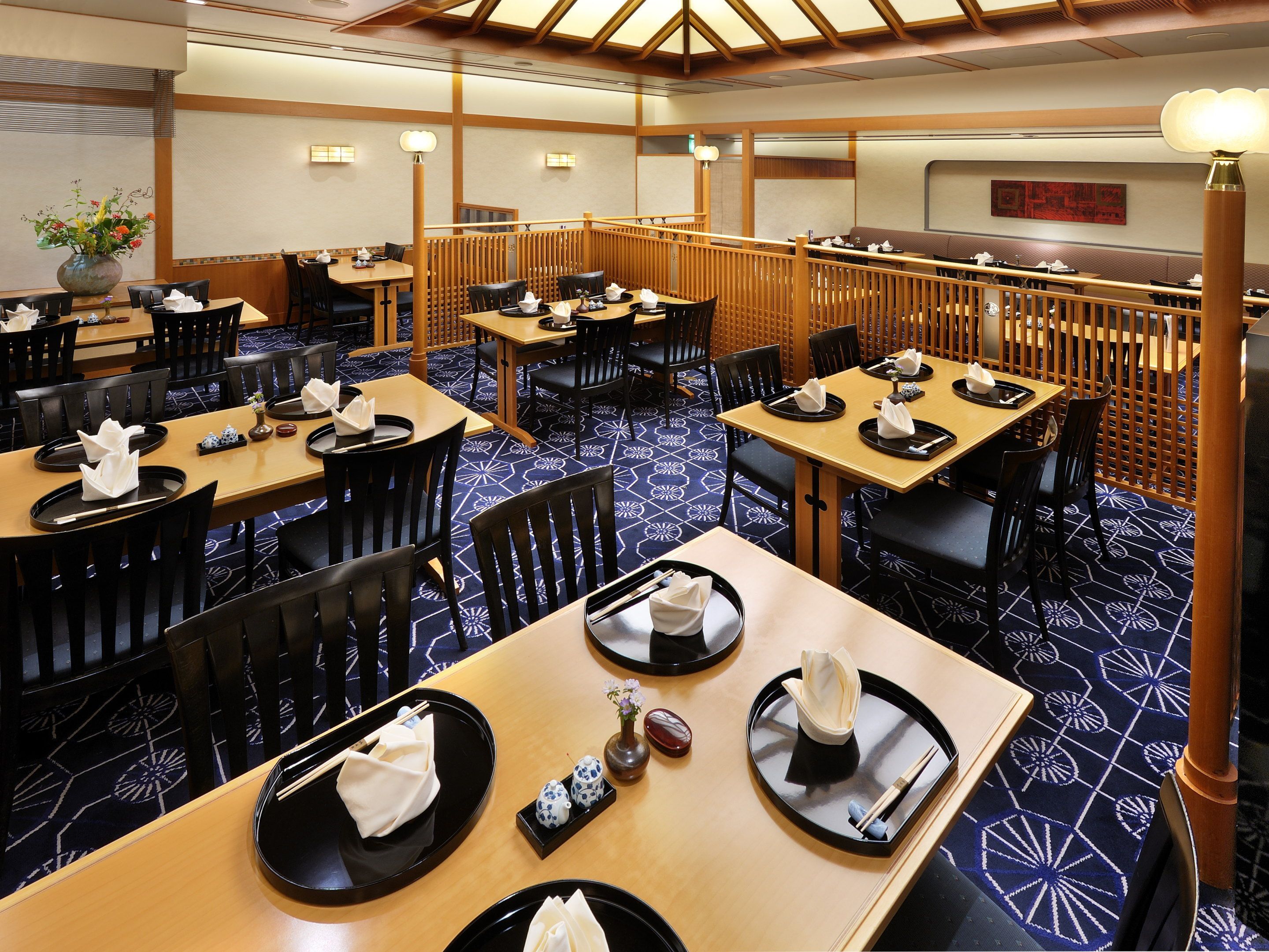 A restaurant with wooden tables and chairs, arranged in a spacious layout with high ceilings and patterned flooring.