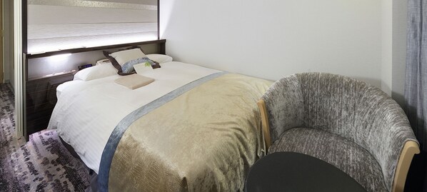 A hotel room with a bed, a bedside table, a chair, and a window with blinds.